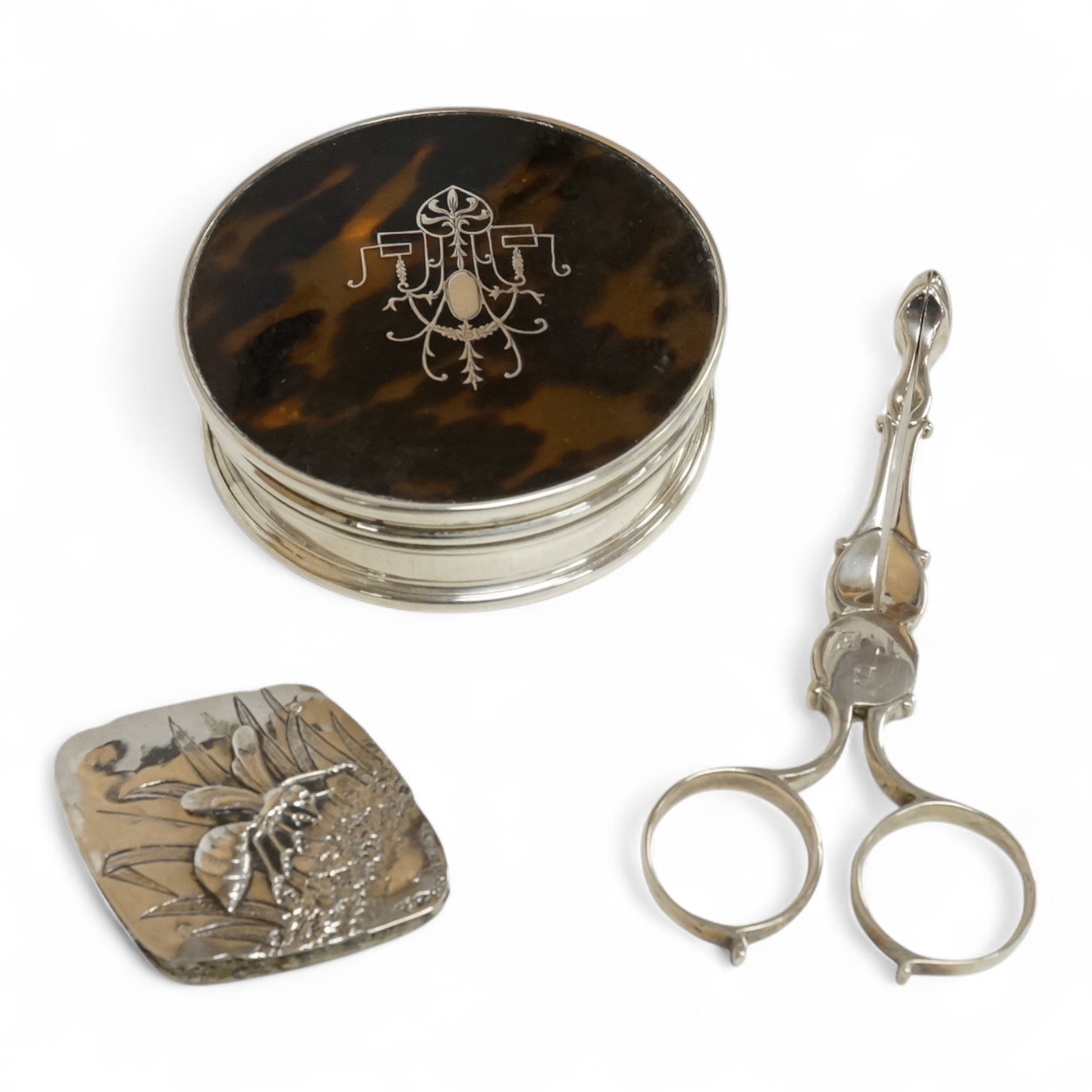 A George V silver and tortoiseshell pique mounted circular trinket box, Collett & Anderson, London, 1922, diameter 77mm, together with a pair of 18th century silver sugar nips and a sterling mounted pin cushion, decorate